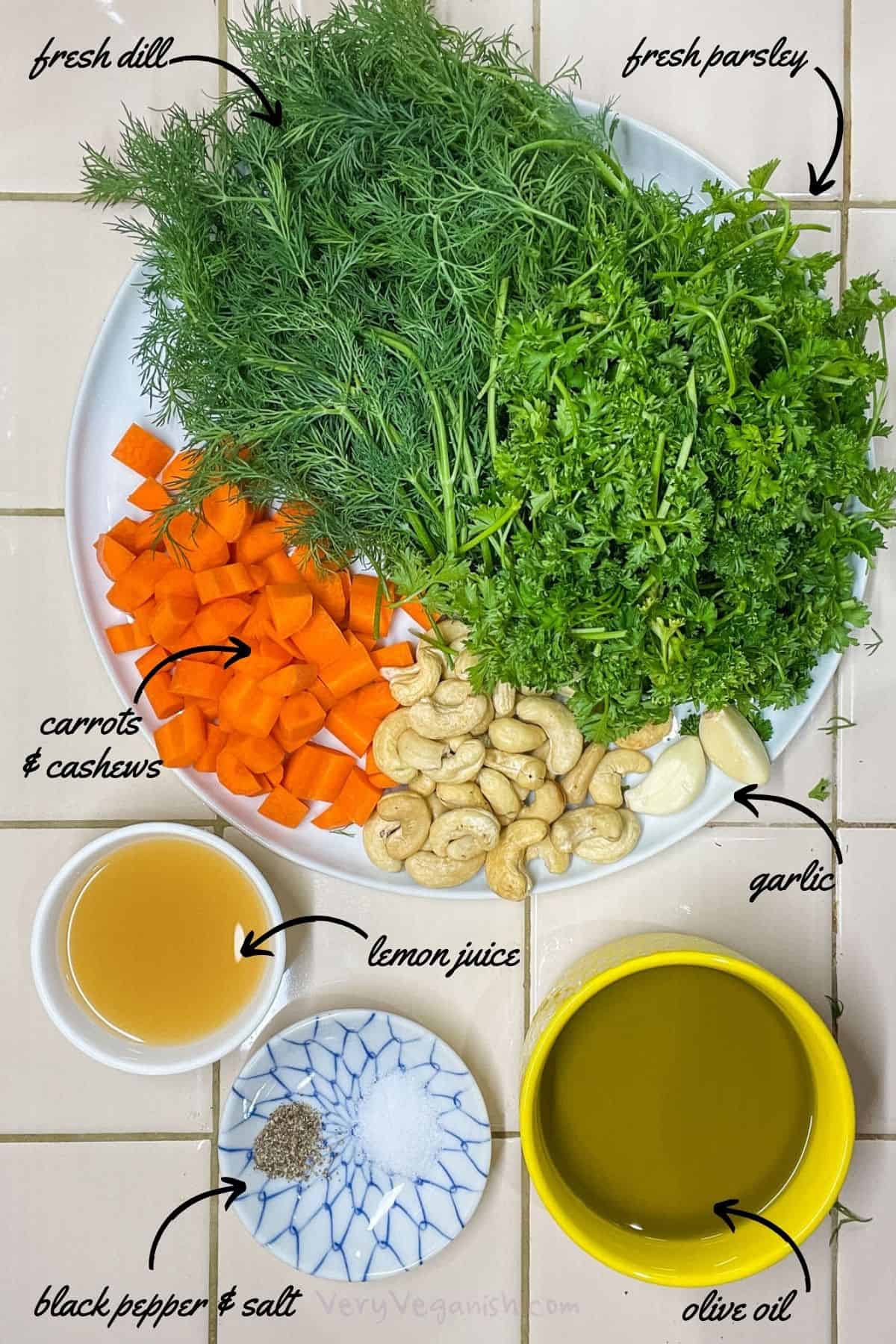 Ingredients for Carrot Cashew Dill Parsley Pesto Recipe on counter: fresh dill, fresh parsley, chopped carrots, raw cashews, garlic cloves, lemon juice, olive oil, salt and black pepper