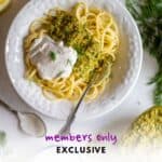 Spaghetti with dill parsley pesto and vegan sour cream in a white bowl with a fork on the side