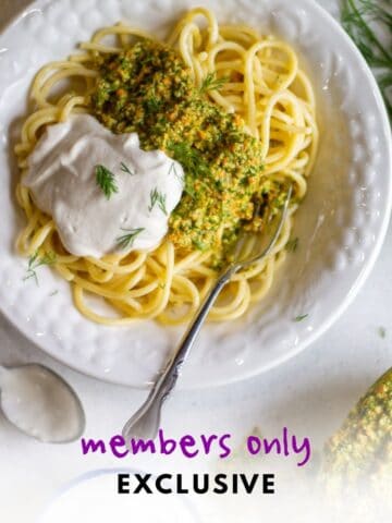 Spaghetti with dill parsley pesto and vegan sour cream in a white bowl with a fork on the side