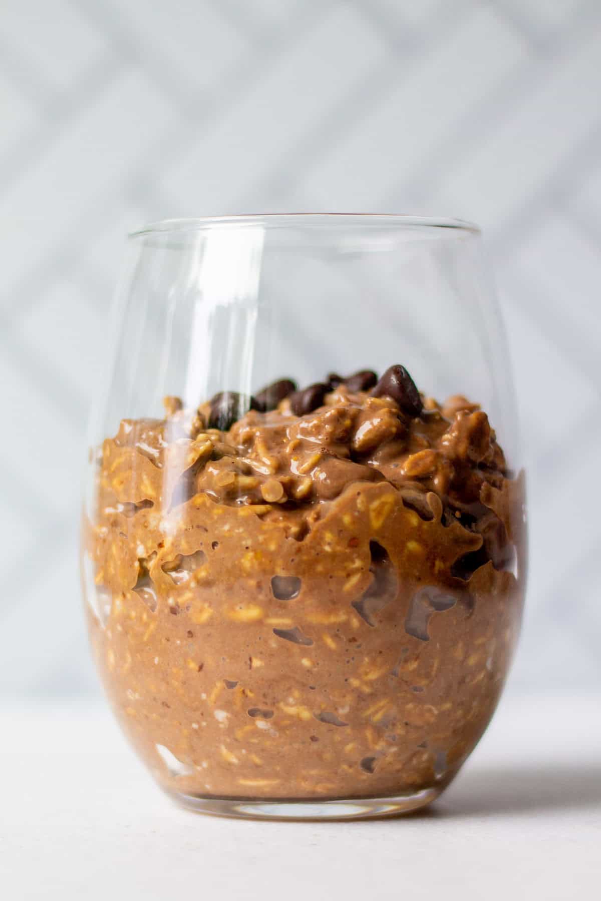 Side view of creamy vegan double chocolate overnight oats in a glass, showing thick texture with oats and chocolate chips.