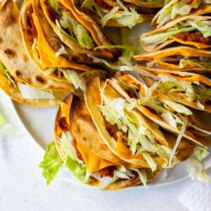 Close-up of crispy vegan Jack in the Box tacos copycat filled with soy chorizo, shredded lettuce, and melty vegan cheese in toasted corn tortillas.