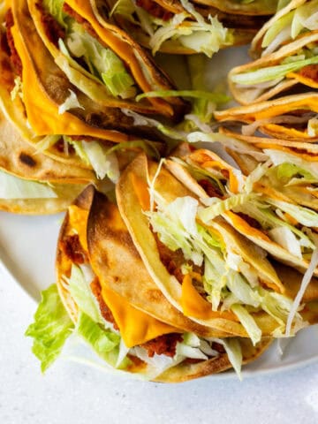 Close-up of crispy vegan Jack in the Box tacos copycat filled with soy chorizo, shredded lettuce, and melty vegan cheese in toasted corn tortillas.