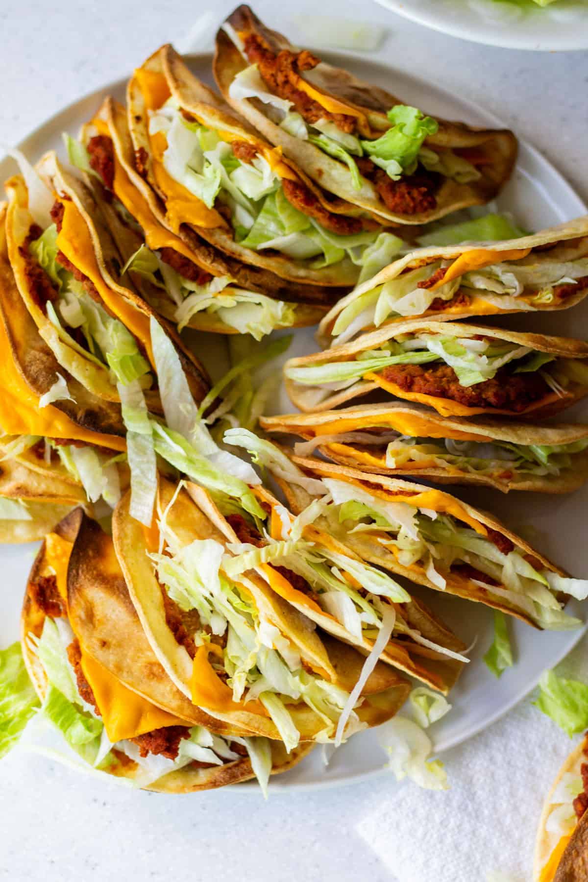 Plate of crispy vegan Jack in the Box tacos copycat made with soy chorizo, shredded lettuce, and melted vegan cheese in golden corn tortillas.