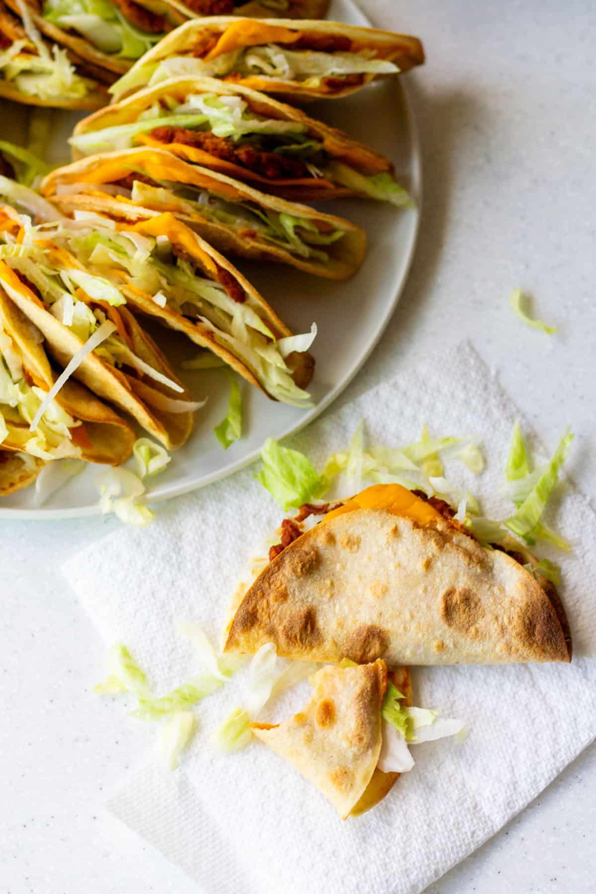 Crispy vegan Jack in the Box tacos copycat with shredded lettuce and vegan cheese, one taco broken open on a napkin to show the filling.