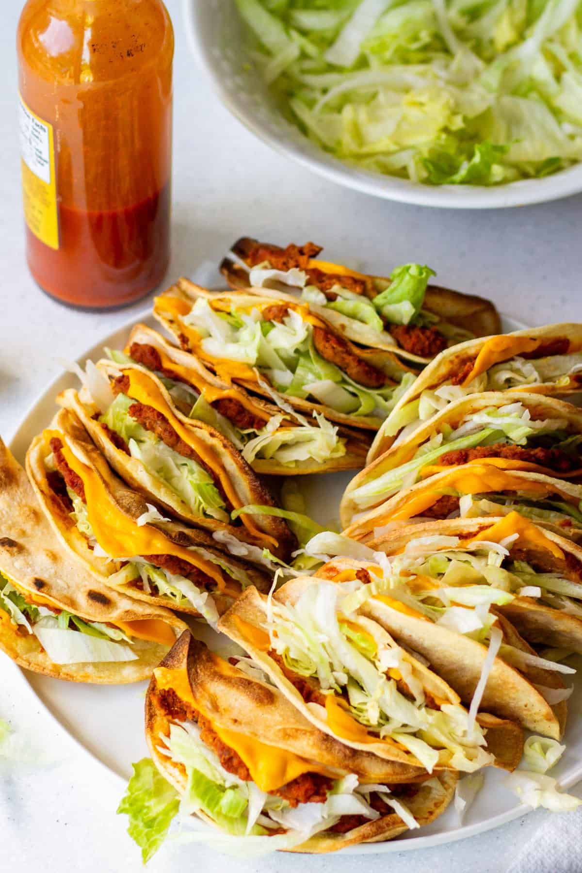 Plate of vegan Jack in the Box tacos copycat recipe topped with shredded lettuce and vegan cheese, served with hot sauce on the side.