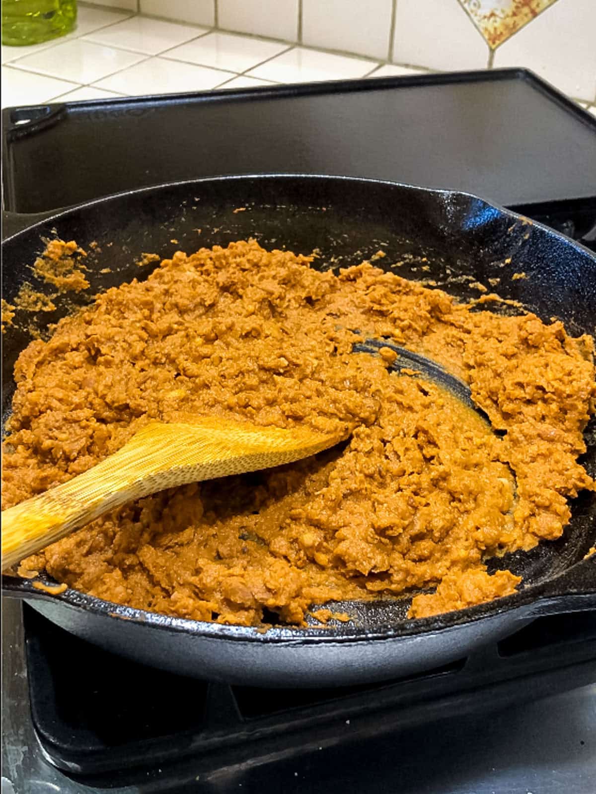 Mixing cooked soy chorizo with refried beans in a skillet for vegan taco filling.