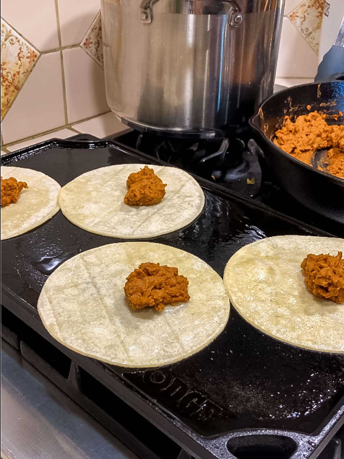Adding vegan taco filling to corn tortillas on a griddle for copycat Jack in the Box tacos.