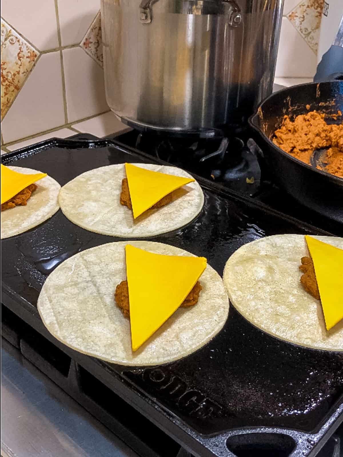 Placing slices of vegan cheese on tortillas with taco filling while cooking on griddle.