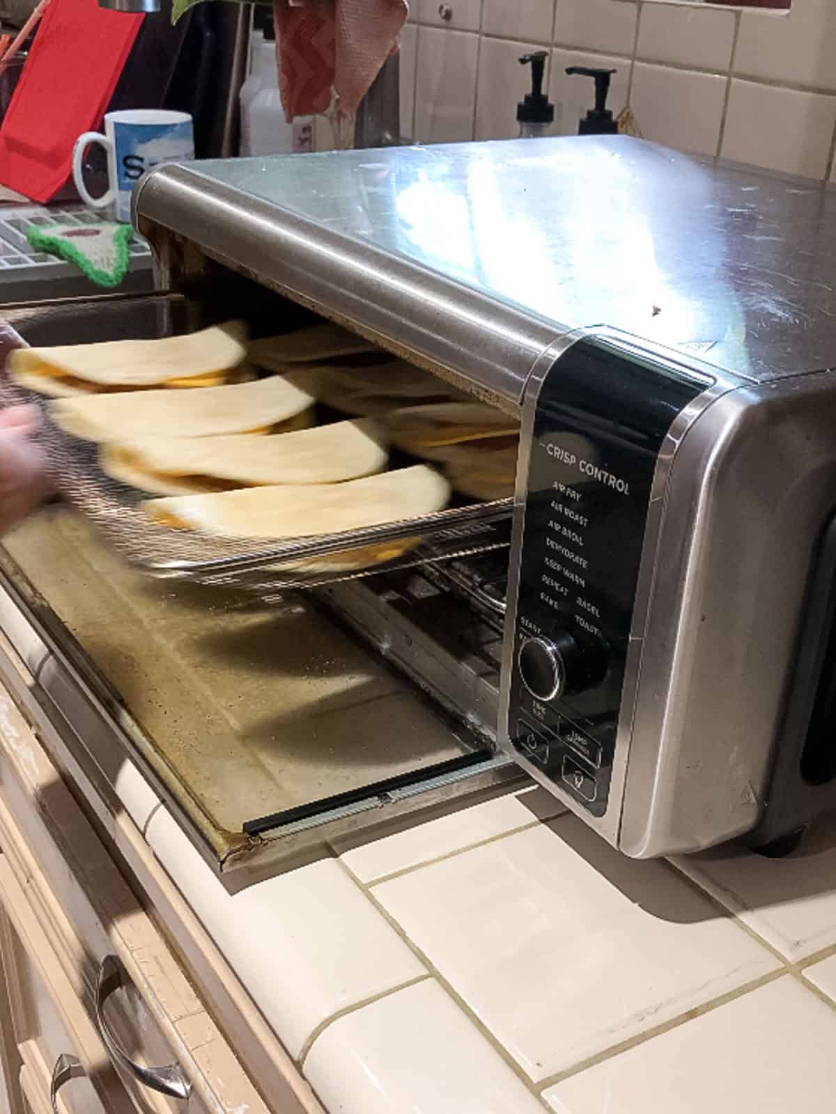 Loading folded vegan tacos into toaster oven air fryer to crisp shells.