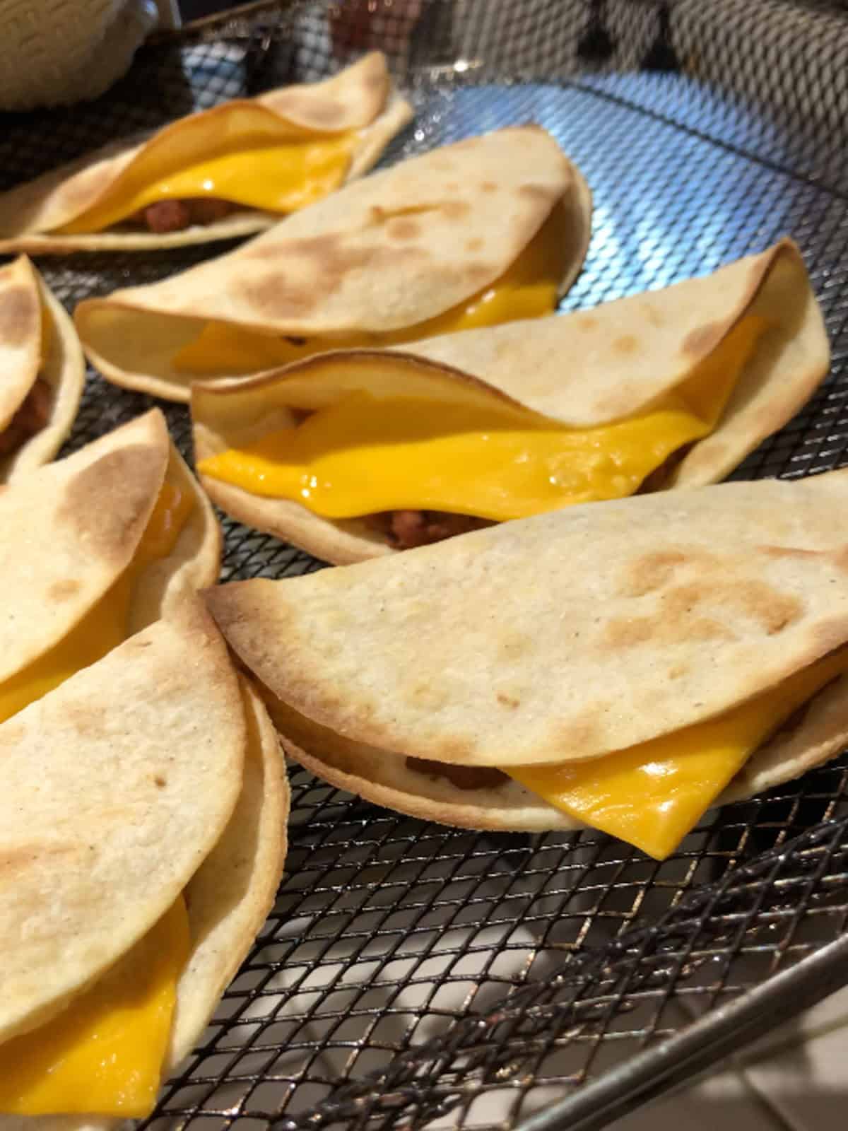 Crispy vegan tacos with melted cheese in air fryer basket after cooking.