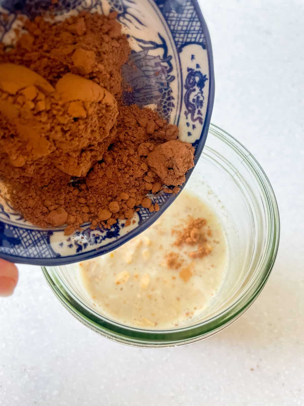 Adding cocoa powder to plant-based milk and oats in a jar for vegan double chocolate overnight oats.