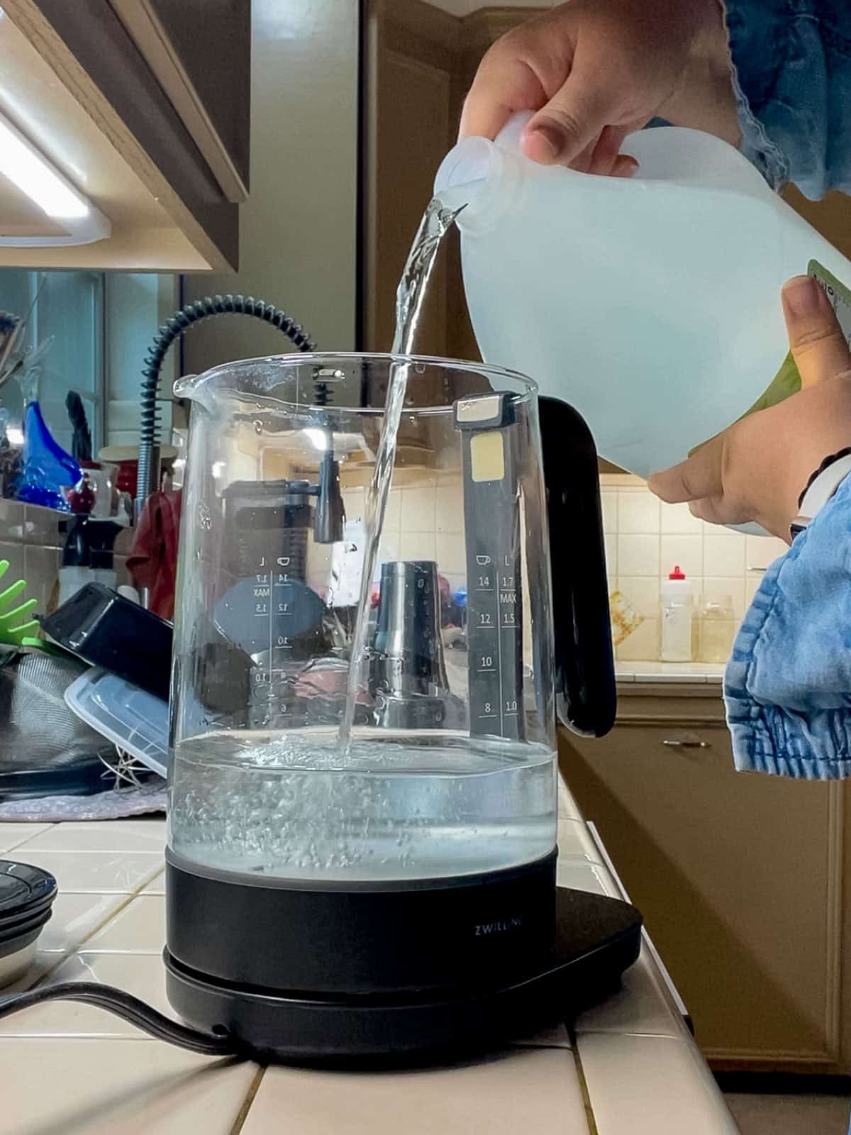 Pouring distilled white vinegar into an electric kettle as the first step to remove mineral buildup and limescale without scrubbing.