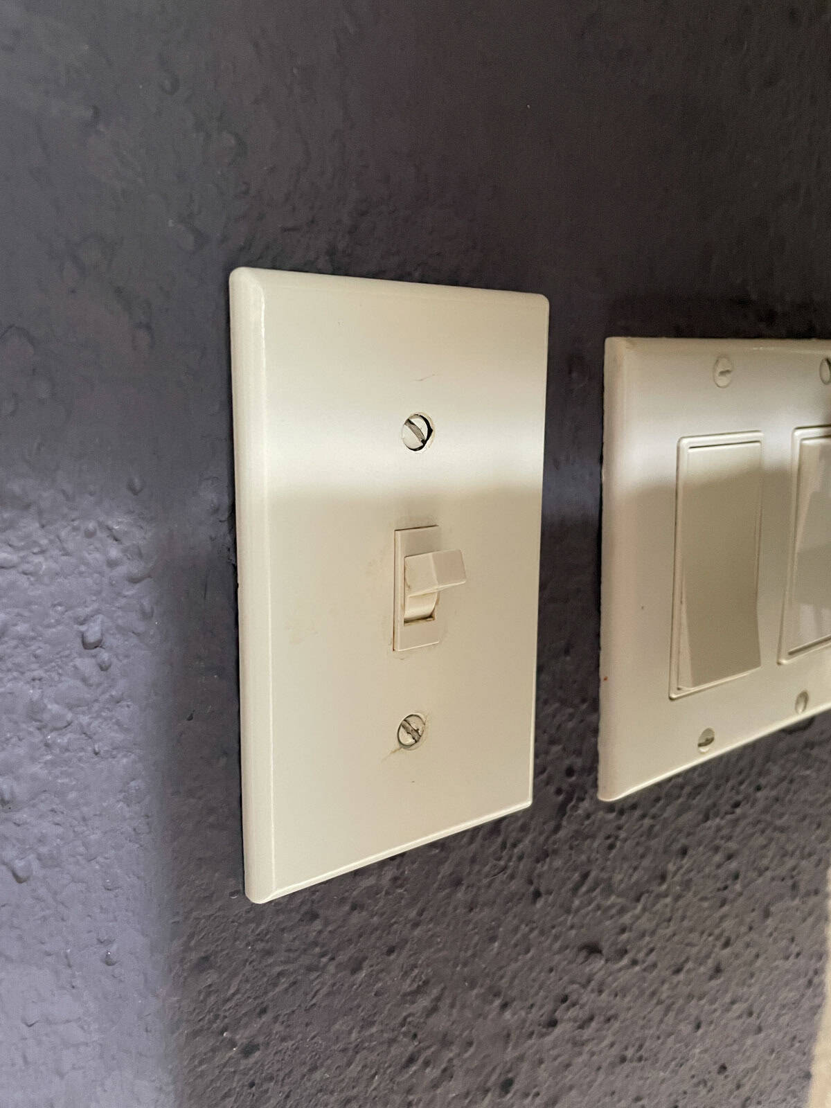 Side view of a bathroom light switch installed on a textured wall finished with James Alexander Natural Paint, showing the paint’s durability after one year.