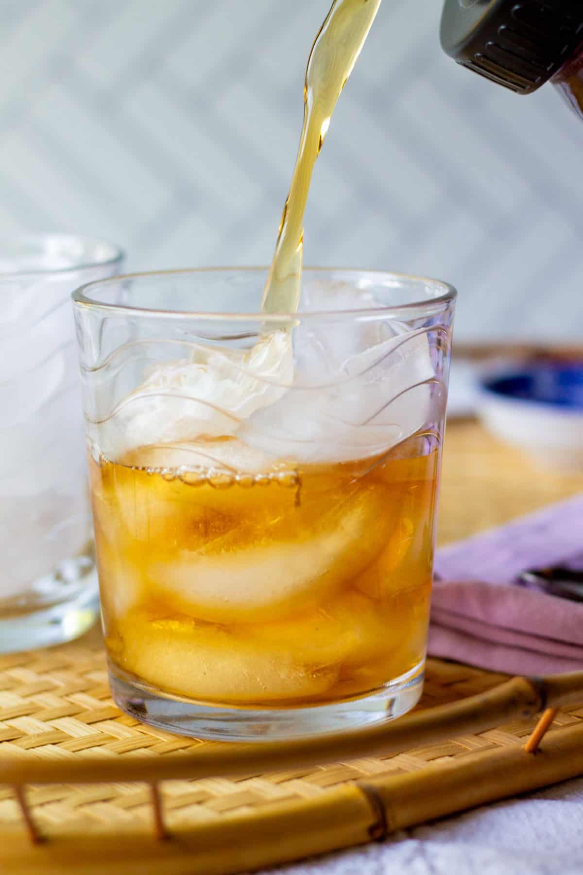 Pouring homemade rooibos iced tea made with loose leaf tea into a glass filled with ice cubes.