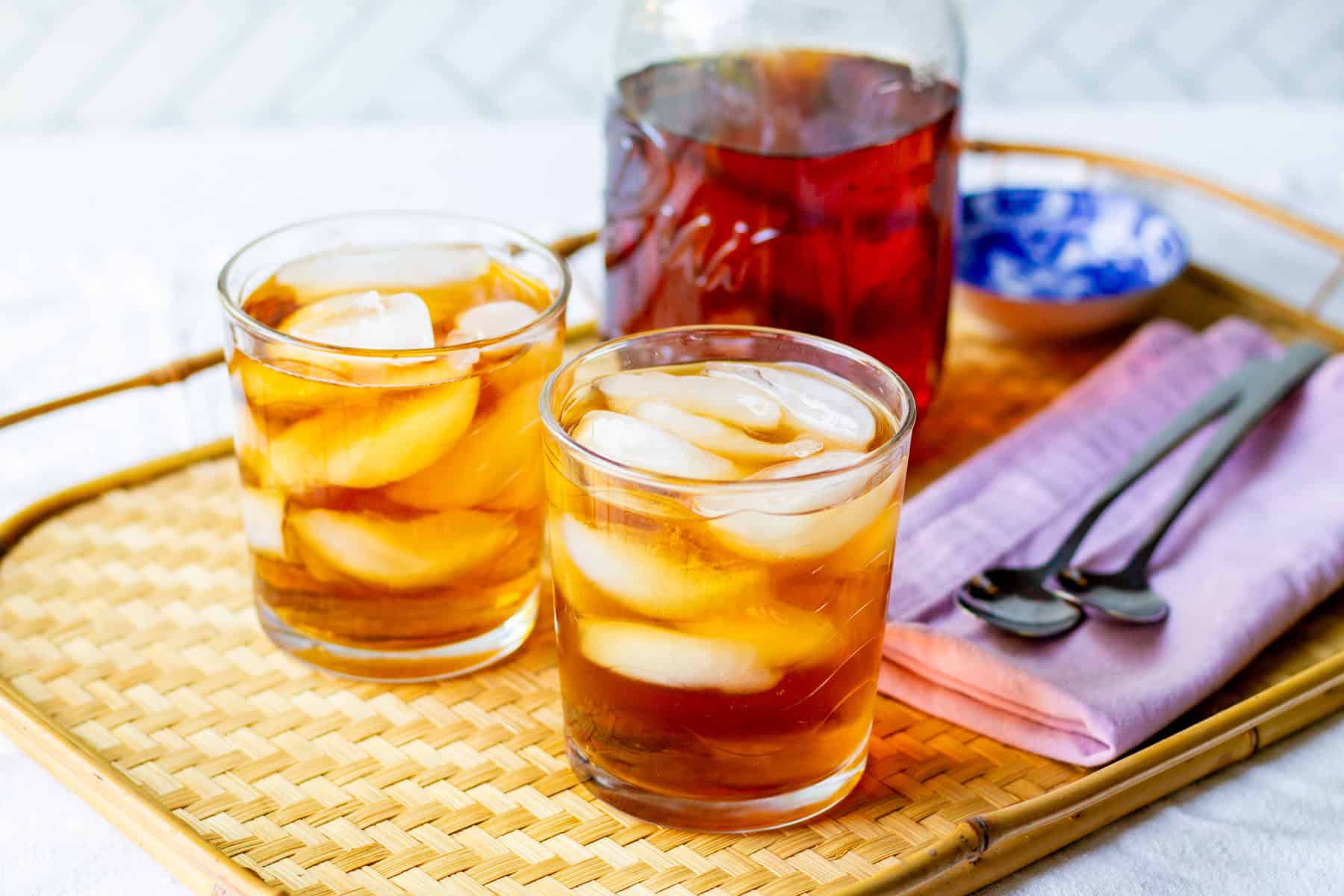 Two glasses of rooibos iced tea made with loose leaf tea served over ice on a woven serving tray.
