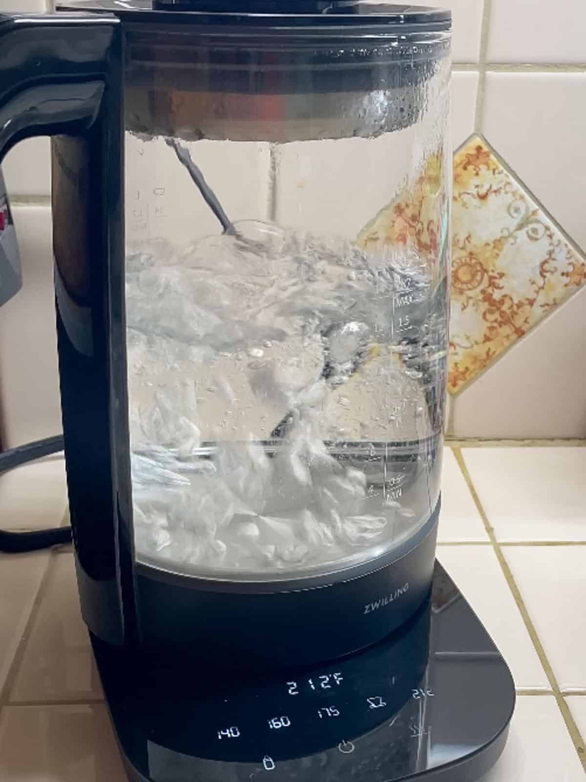 Glass electric kettle boiling water for making homemade rooibos iced tea with tea bags.