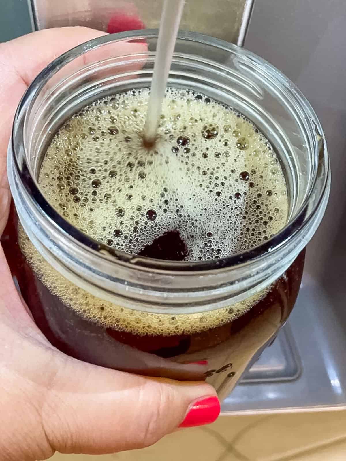 Cold water being added to concentrated rooibos tea in a mason jar to make homemade rooibos iced tea with tea bags.