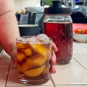 Glass of rooibos iced tea served over ice beside a mason jar of freshly brewed rooibos tea concentrate.