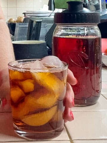 Glass of rooibos iced tea served over ice beside a mason jar of freshly brewed rooibos tea concentrate.