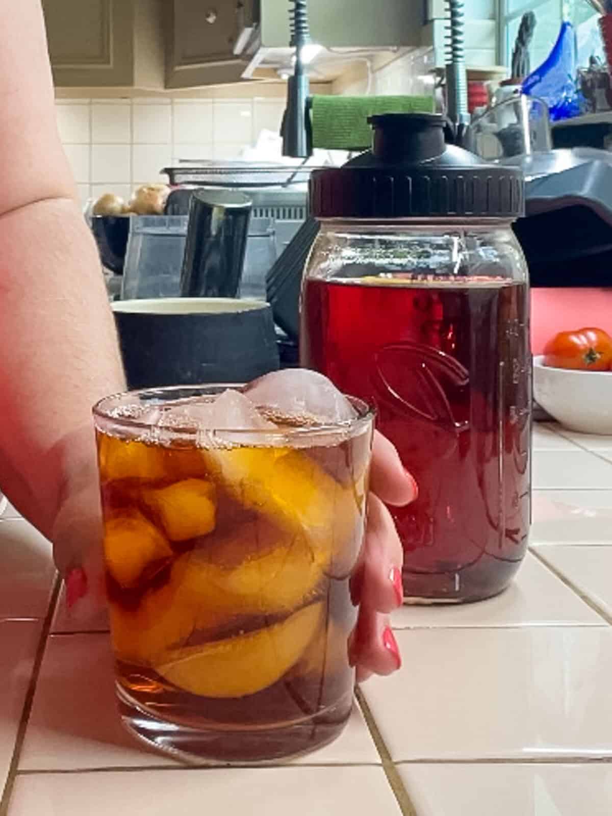 Glass of rooibos iced tea served over ice beside a mason jar of freshly brewed rooibos tea concentrate.