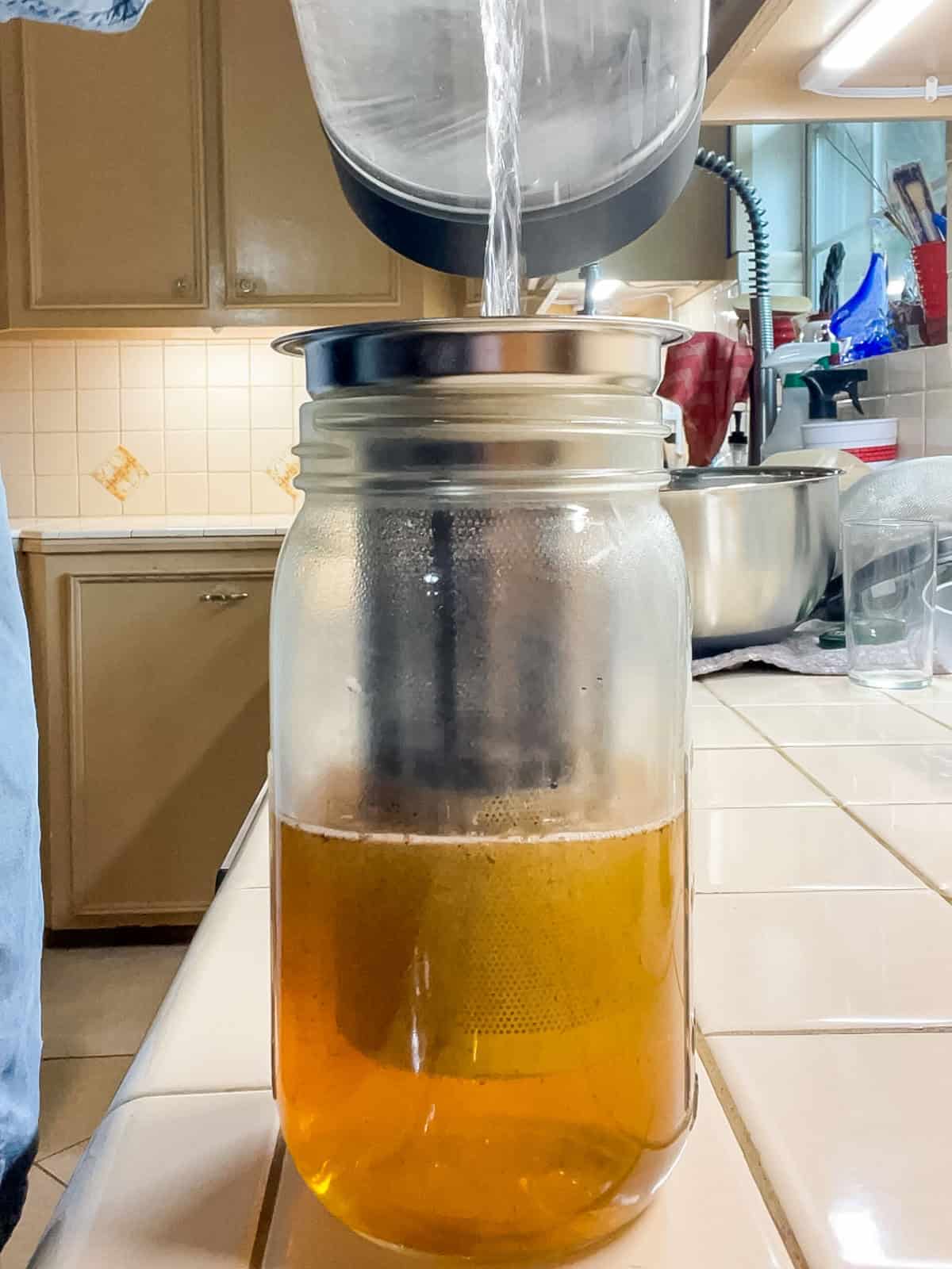 Pouring boiling water over loose leaf rooibos tea in a mason jar to brew homemade iced tea.