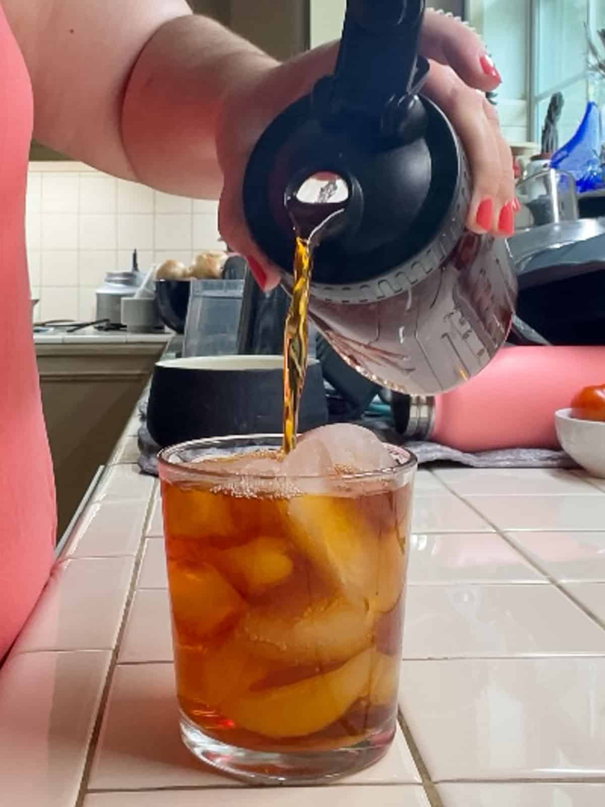 Pouring homemade rooibos iced tea into a glass filled with ice cubes for a refreshing caffeine-free drink.