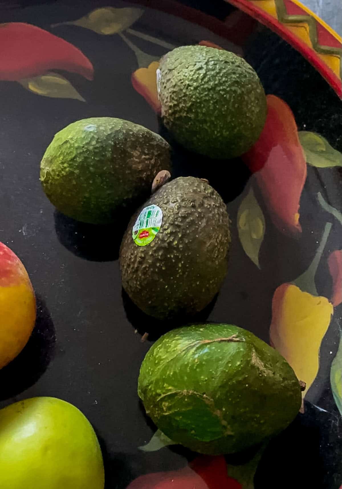 Hard unripe Hass avocados ripening at room temperature in a fruit bowl before using the avocado storage hack.